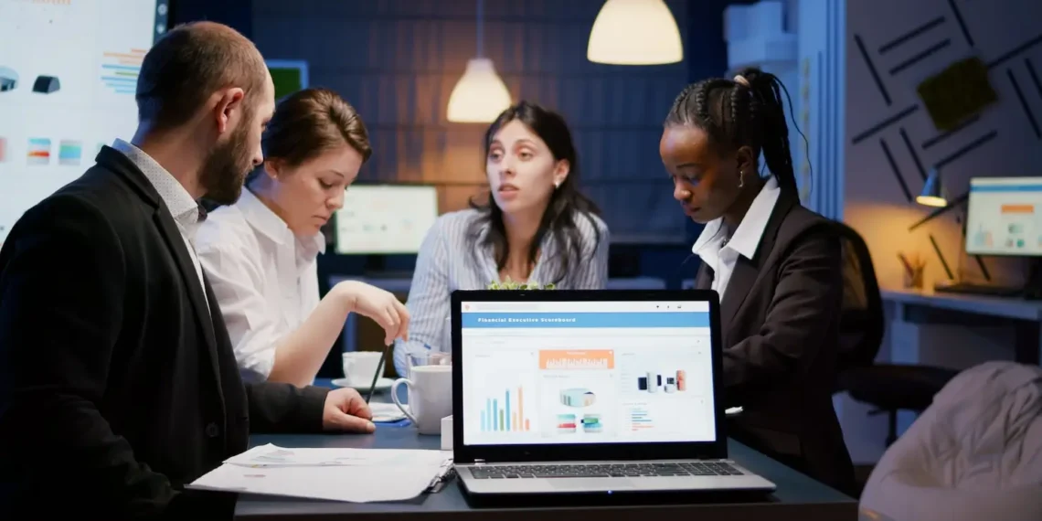 Laptop computer with financial graphs presentation on monitor standing on conference table in meeting room late at night