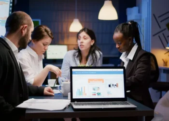 Laptop computer with financial graphs presentation on monitor standing on conference table in meeting room late at night